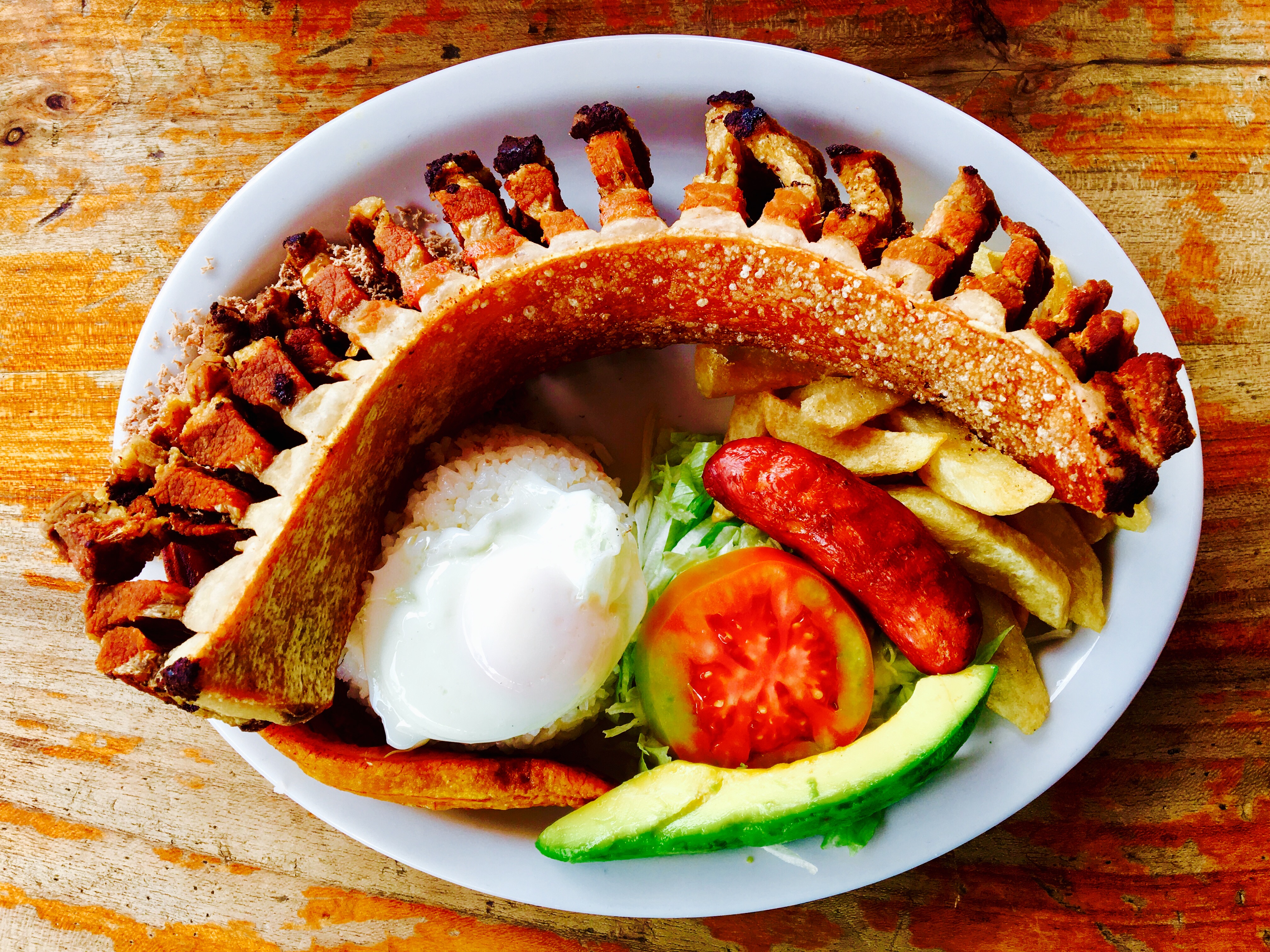 a bandeja paisa with chicharrón avocado egg chorizo potatoes and salad